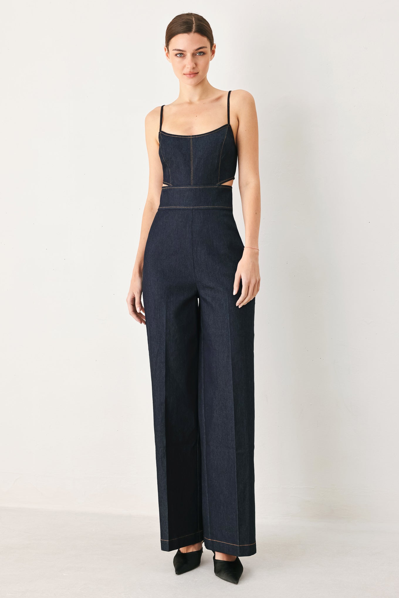 Woman wearing a dark denim jumpsuit  jumpsuit featuring U neckline, straps, side cut out, wide leg and back zipper closure | FREEMARKET