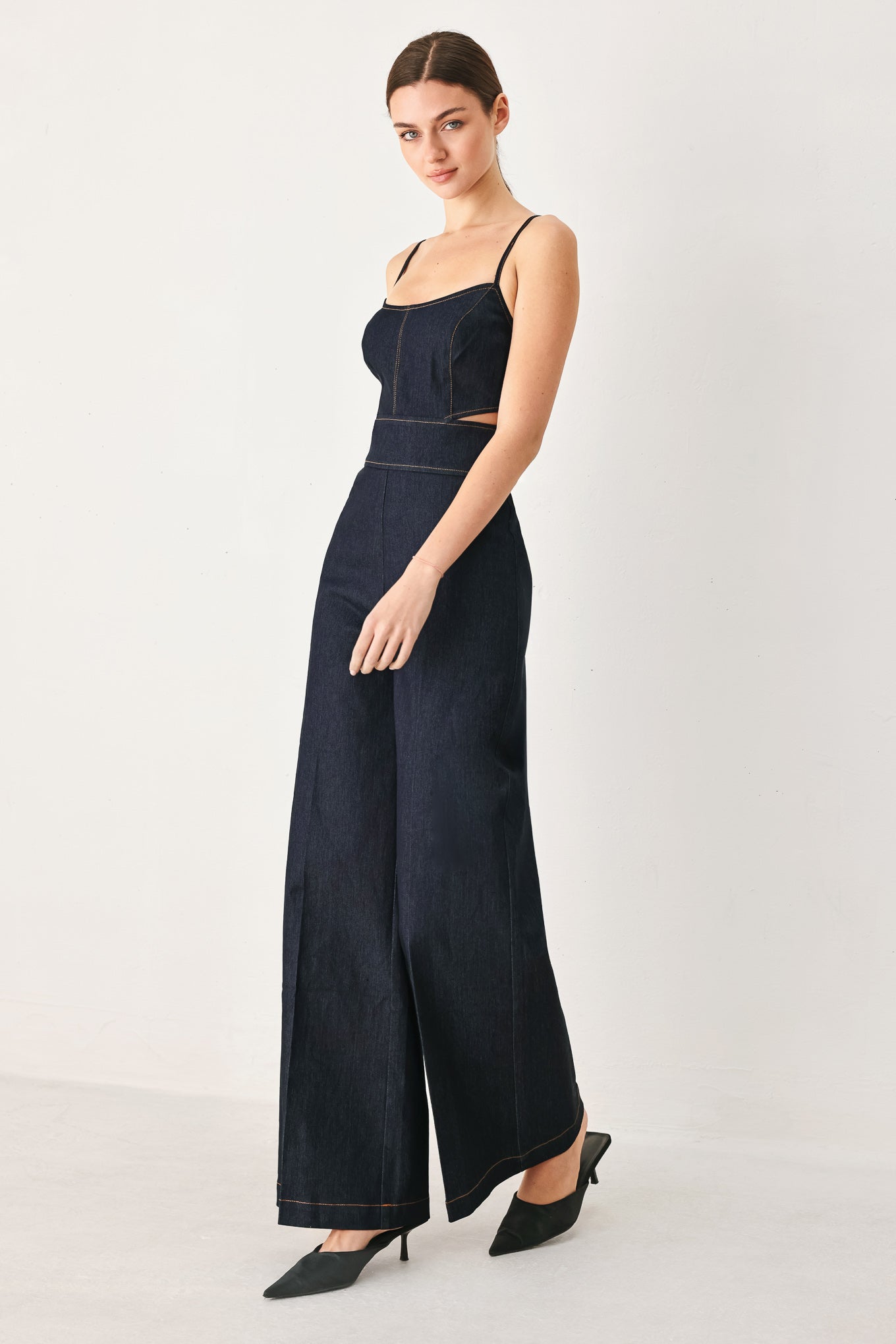Woman wearing a dark denim jumpsuit  jumpsuit featuring U neckline, straps, side cut out, wide leg and back zipper closure | FREEMARKET