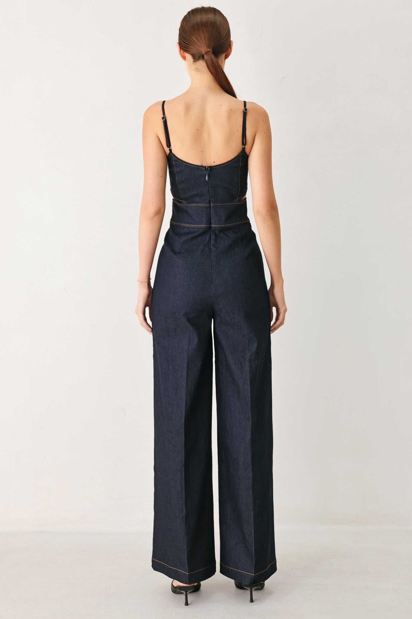 Woman wearing a dark denim jumpsuit  jumpsuit featuring U neckline, straps, side cut out, wide leg and back zipper closure | FREEMARKET