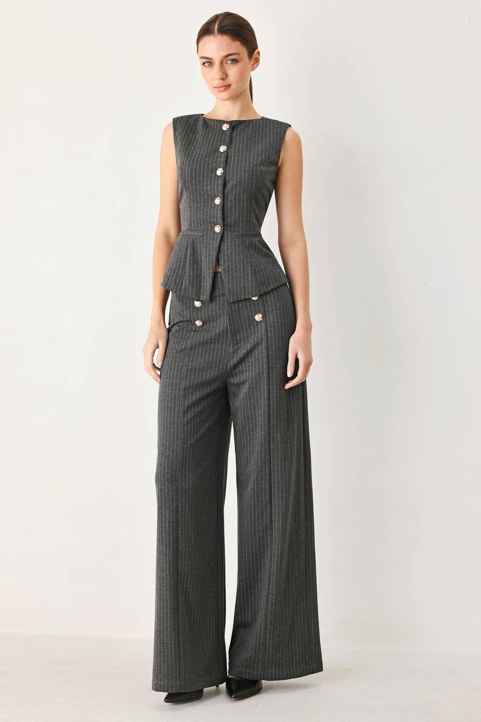 Woman wearing high-waisted, wide-leg charcoal gray and white pinstriped trousers with decorative gold-tone buttons on the front waistband | FREEMARKET