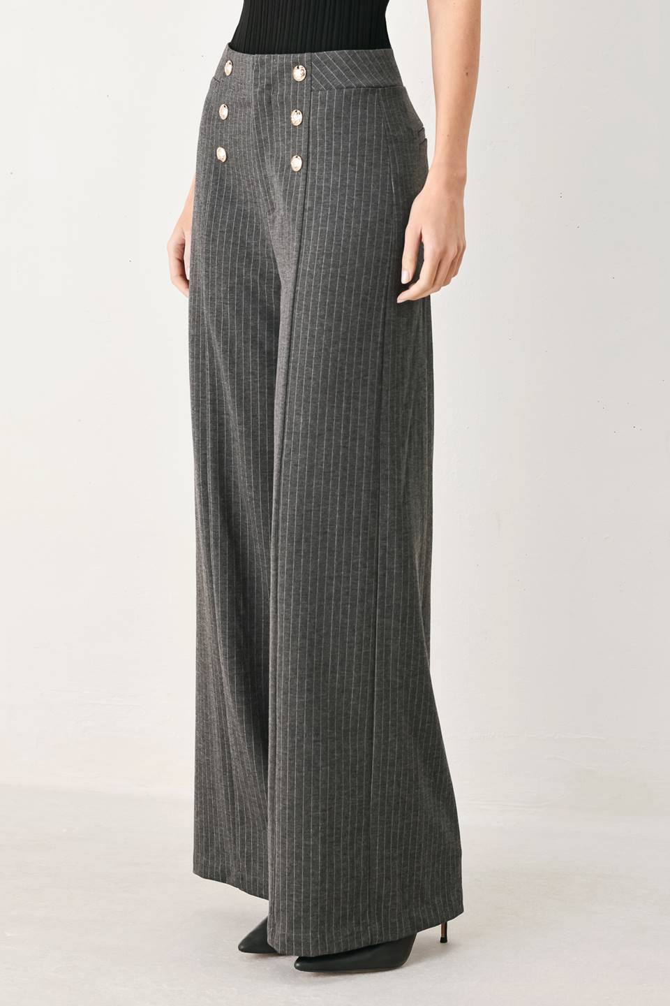 Woman wearing high-waisted, wide-leg charcoal gray and white pinstriped trousers with decorative gold-tone buttons on the front waistband | FREEMARKET
