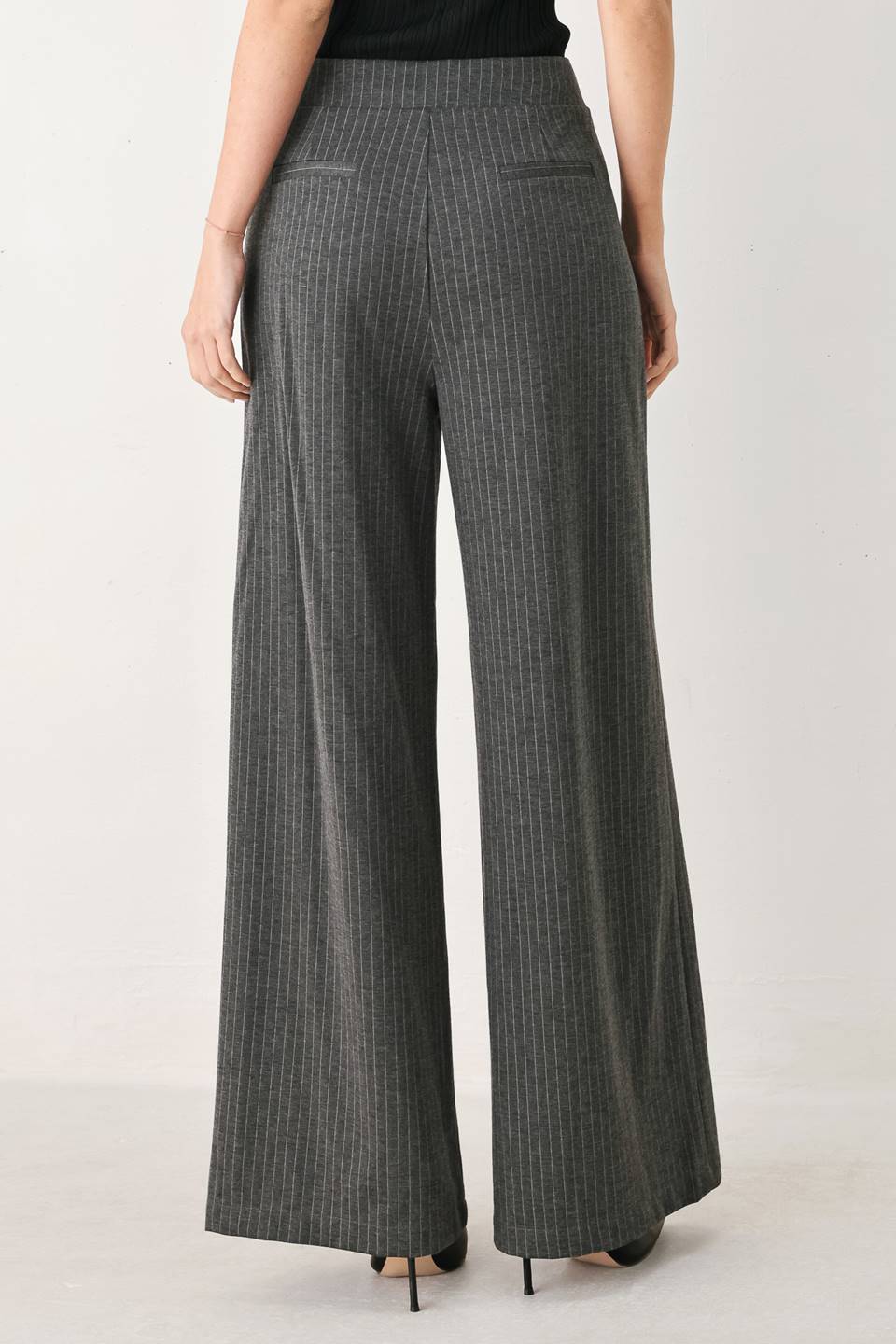 Woman wearing high-waisted, wide-leg charcoal gray and white pinstriped trousers with decorative gold-tone buttons on the front waistband | FREEMARKET