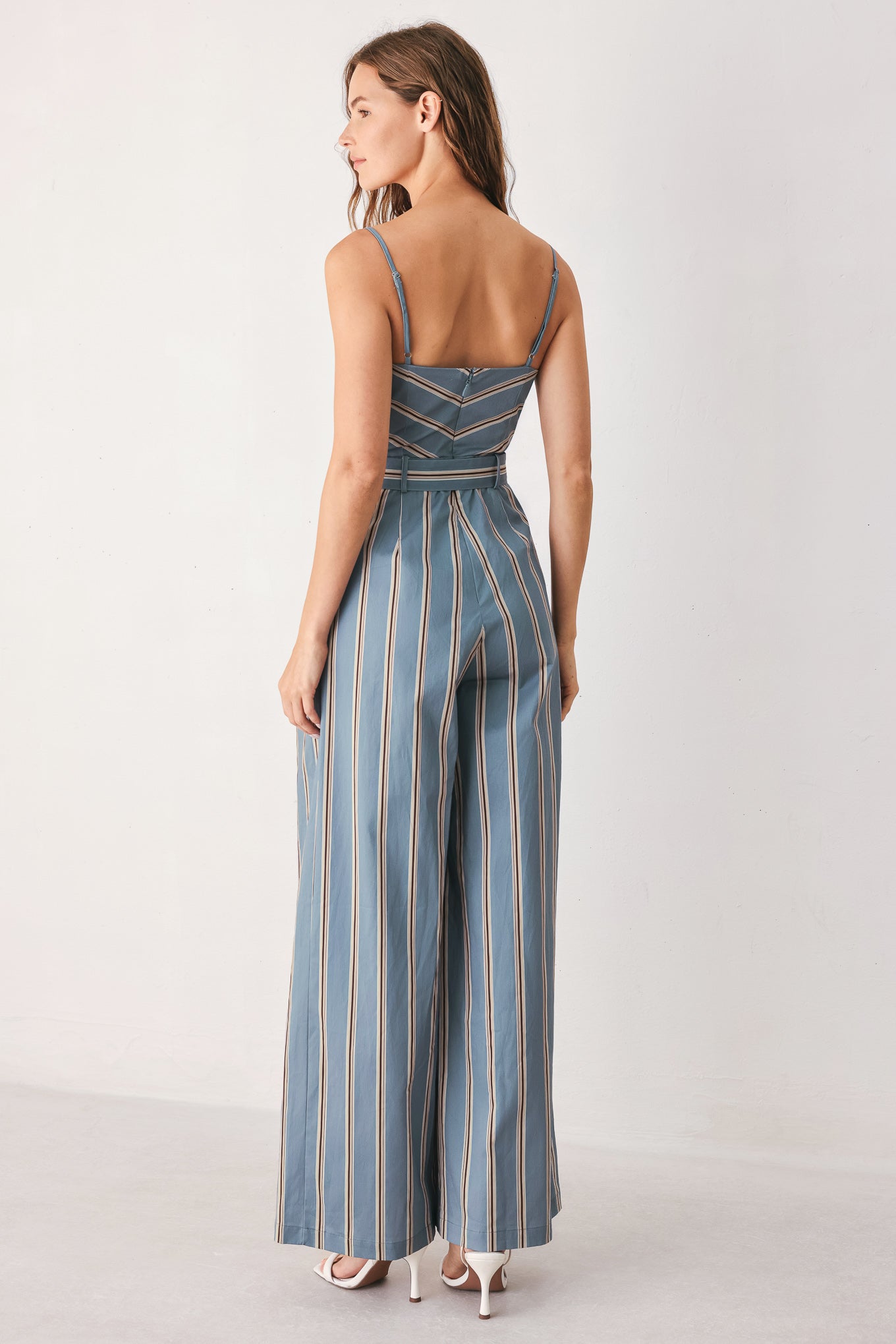 A woman wearing a sleeveless wide-leg jumpsuit with vertical blue, beige, and white stripes, featuring a V-neck bodice, thin shoulder straps, and a matching fabric belt with a silver buckle | FREEMARKET