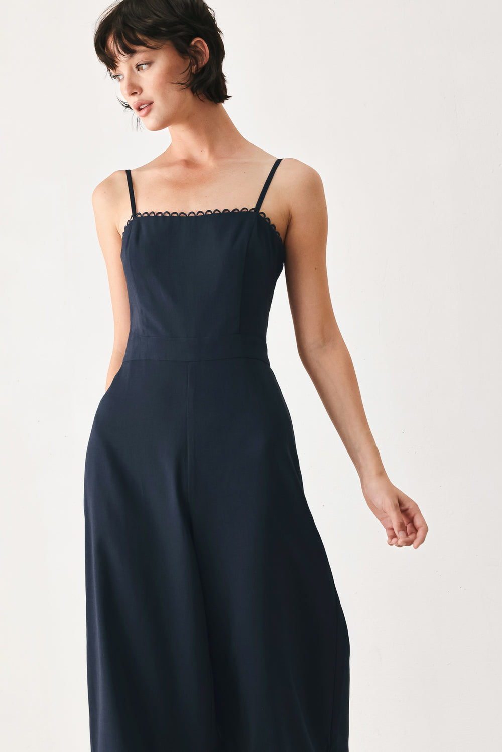 Woman wearing a navy wide leg  jumpsuit straight neckline with trim edge, straps, with lace inset and back zipper closure | FREEMARKET