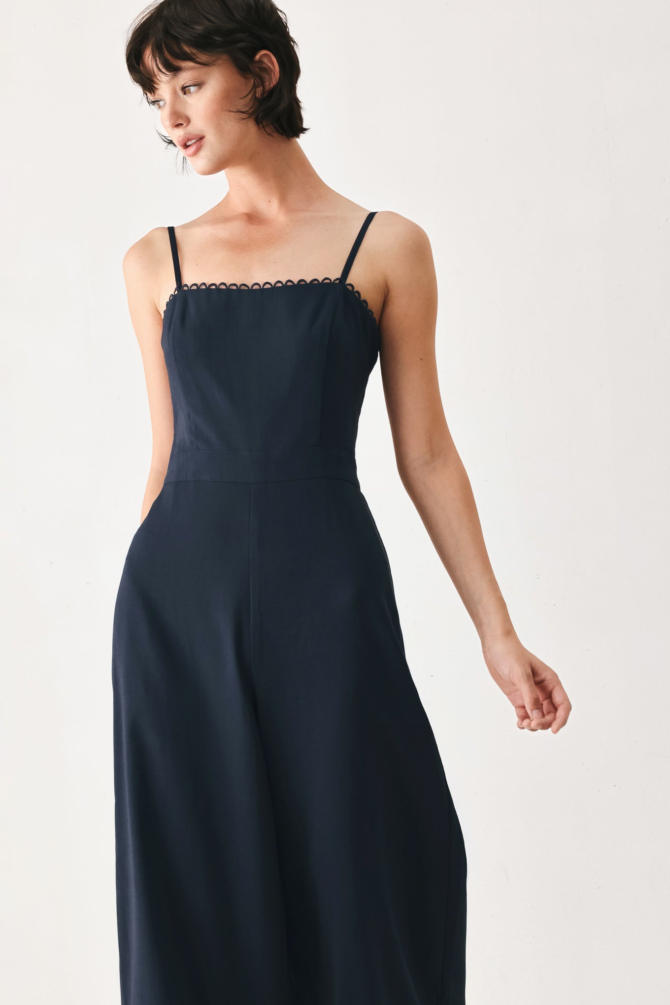 Woman wearing a navy wide leg  jumpsuit straight neckline with trim edge, straps, with lace inset and back zipper closure | FREEMARKET
