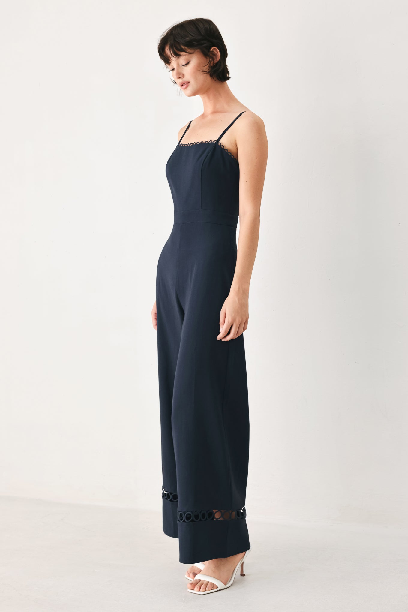 Woman wearing a navy wide leg  jumpsuit straight neckline with trim edge, straps, with lace inset and back zipper closure | FREEMARKET