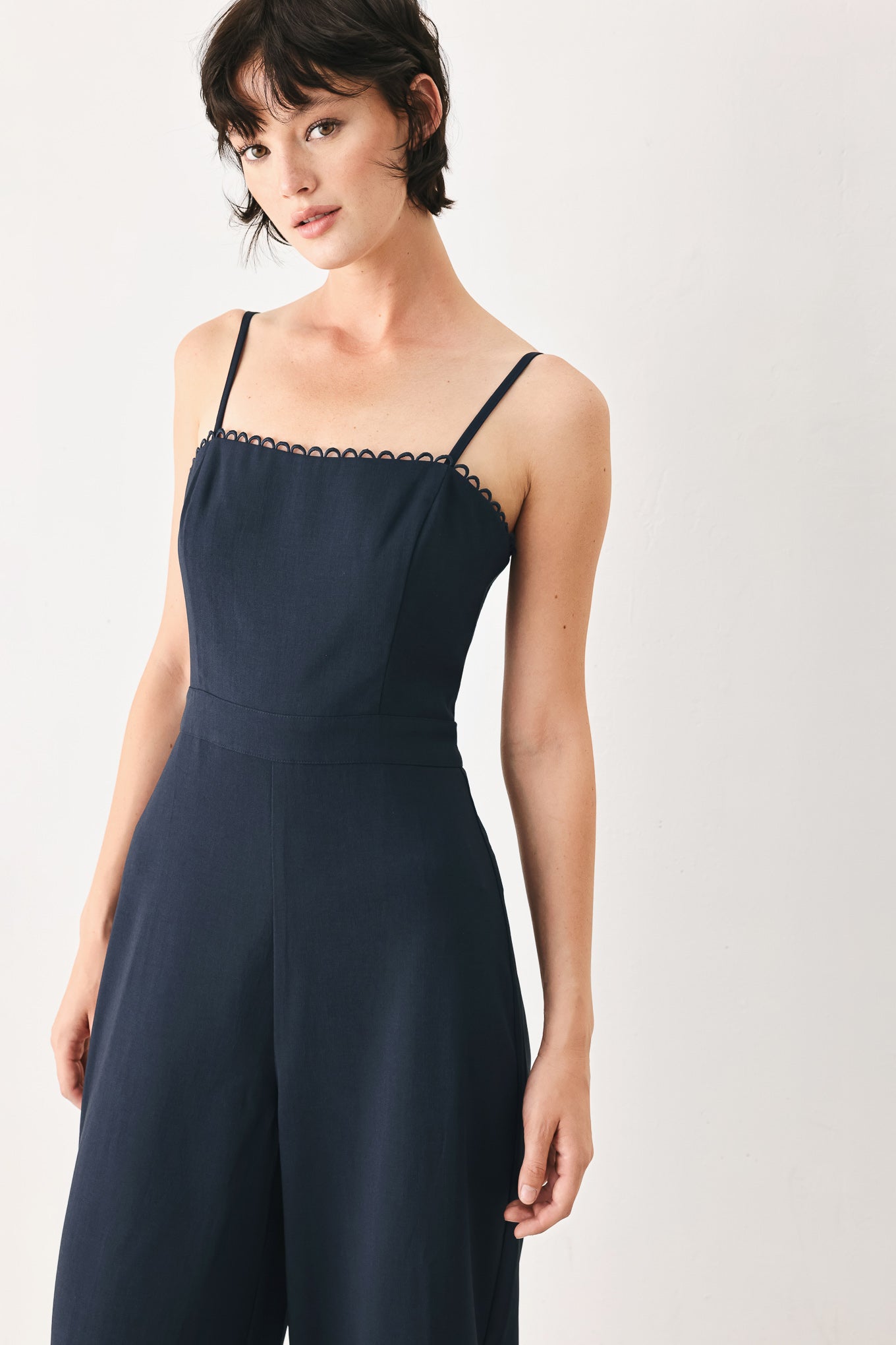 Woman wearing a navy wide leg  jumpsuit straight neckline with trim edge, straps, with lace inset and back zipper closure | FREEMARKET