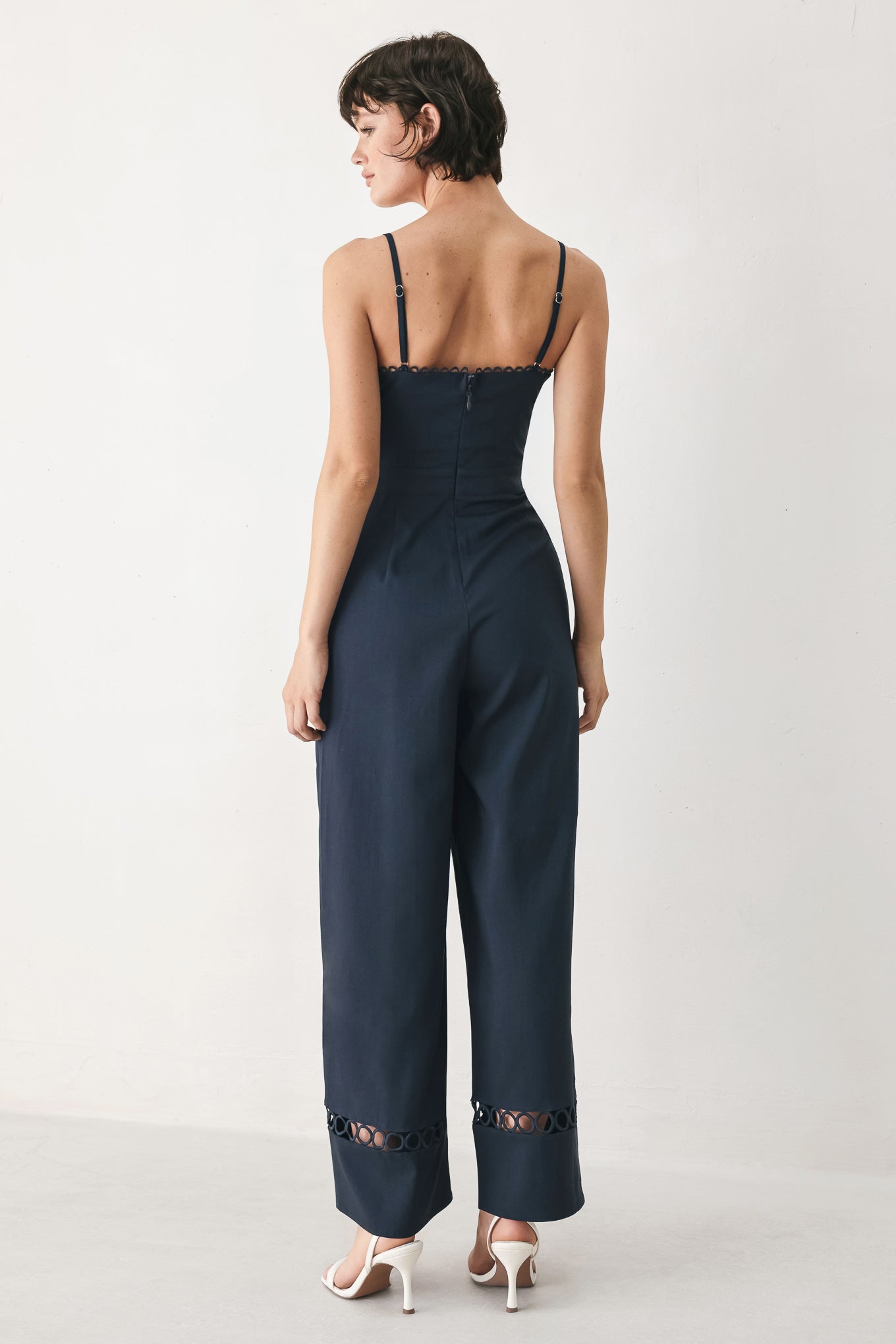 Woman wearing a navy wide leg  jumpsuit straight neckline with trim edge, straps, with lace inset and back zipper closure | FREEMARKET