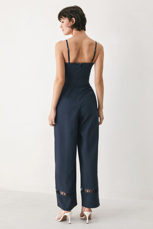 Woman wearing a navy wide leg  jumpsuit straight neckline with trim edge, straps, with lace inset and back zipper closure | FREEMARKET