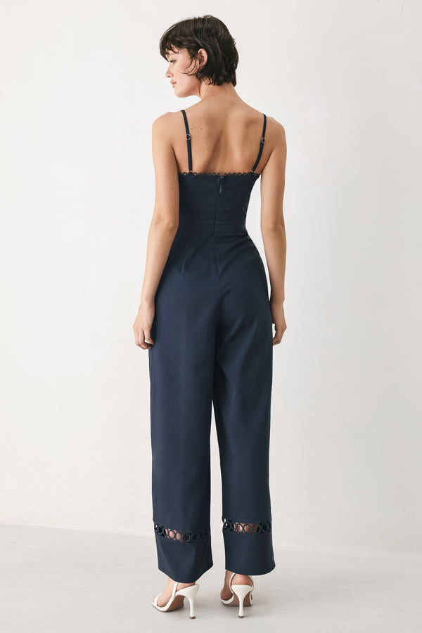 Woman wearing a navy wide leg  jumpsuit straight neckline with trim edge, straps, with lace inset and back zipper closure | FREEMARKET