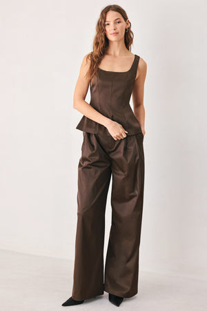 A person wearing high-waisted, wide-leg brown trousers with a glossy finish | FREEMARKET