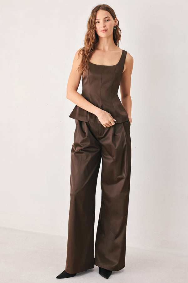 A person wearing high-waisted, wide-leg brown trousers with a glossy finish | FREEMARKET