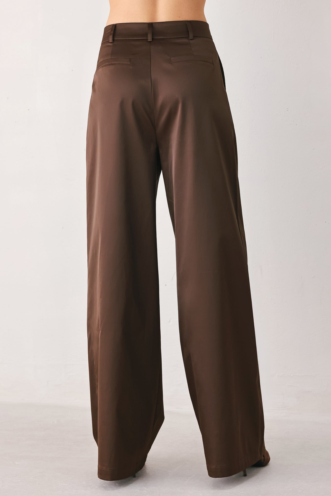 A person wearing high-waisted, wide-leg brown trousers with a glossy finish | FREEMARKET