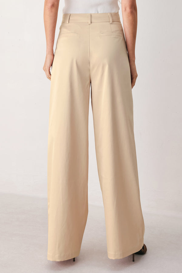 A person wearing high-waisted, wide-leg champagne trousers with a glossy finish | FREEMARKET