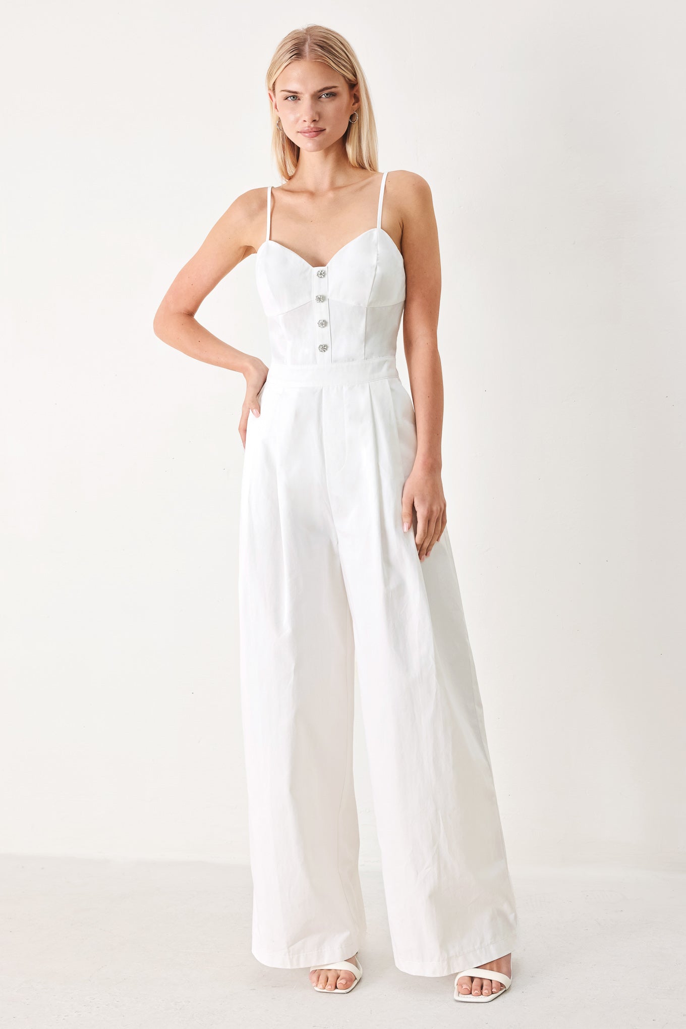 Woman wearing a white jumpsuit with front button detail, straps, side pockets, wide leg and back zipper closure | FREEMARKET