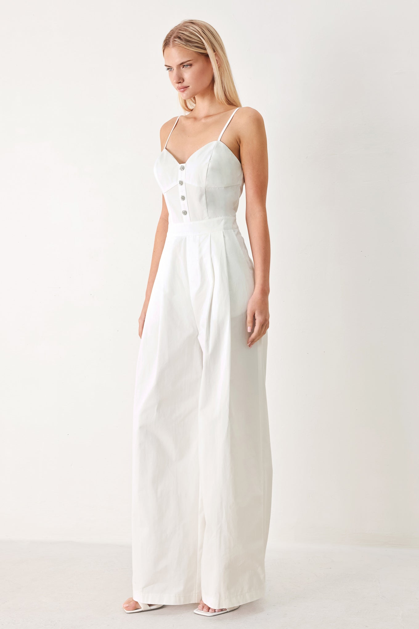 Woman wearing a white jumpsuit with front button detail, straps, side pockets, wide leg and back zipper closure | FREEMARKET