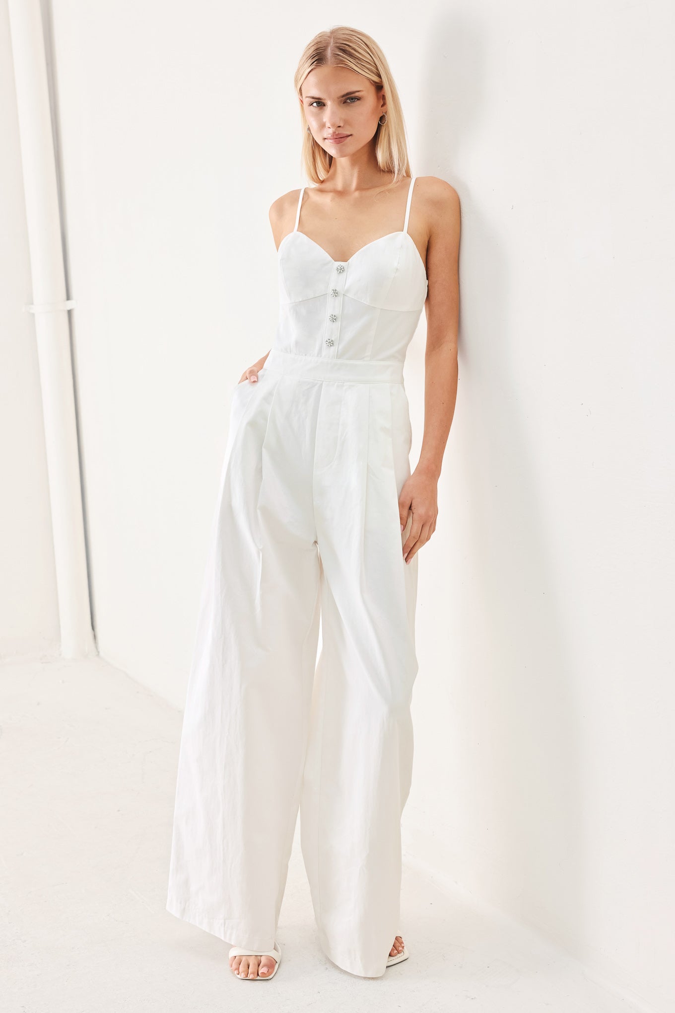 Woman wearing a white jumpsuit with front button detail, straps, side pockets, wide leg and back zipper closure | FREEMARKET