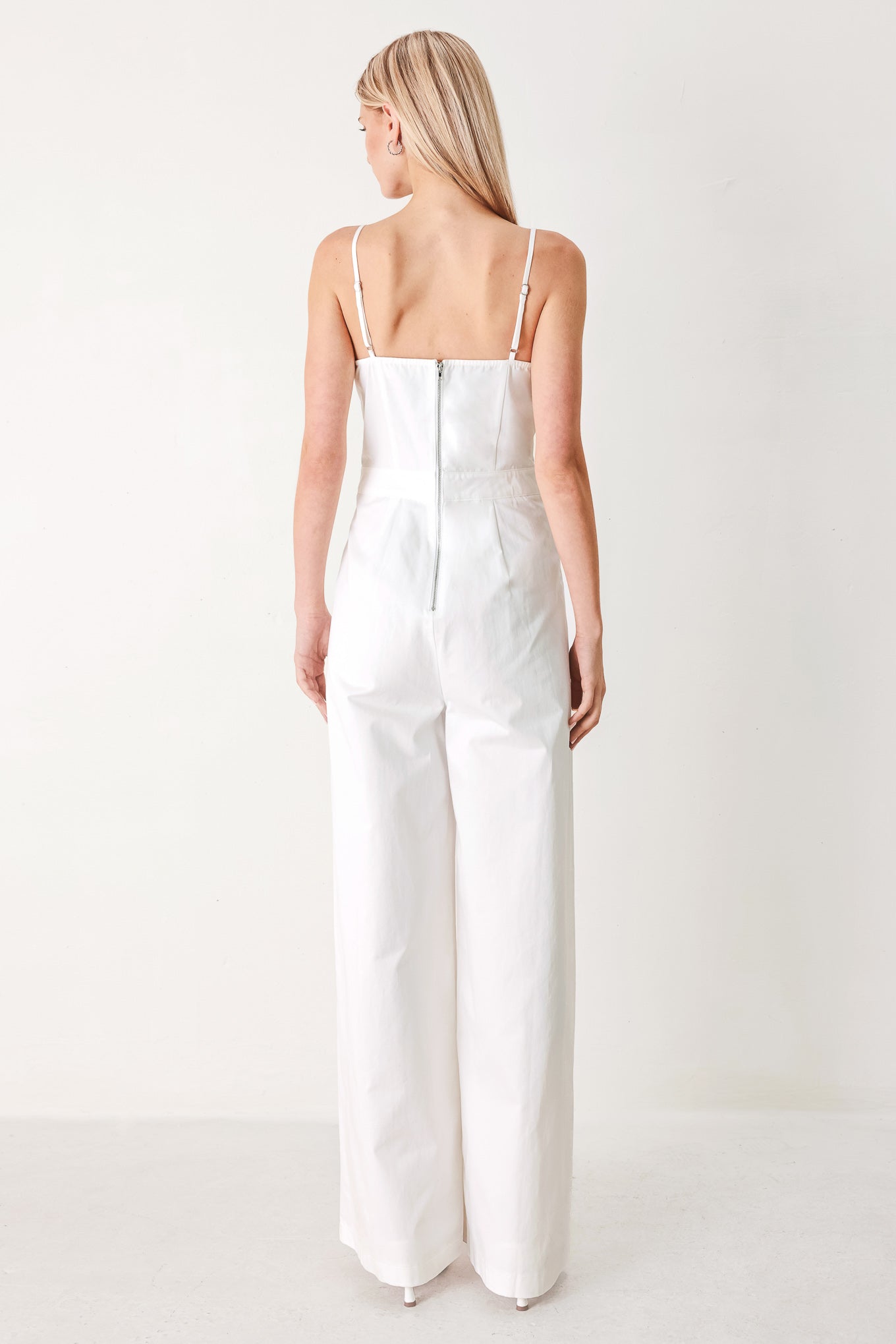 Woman wearing a white jumpsuit with front button detail, straps, side pockets, wide leg and back zipper closure | FREEMARKET