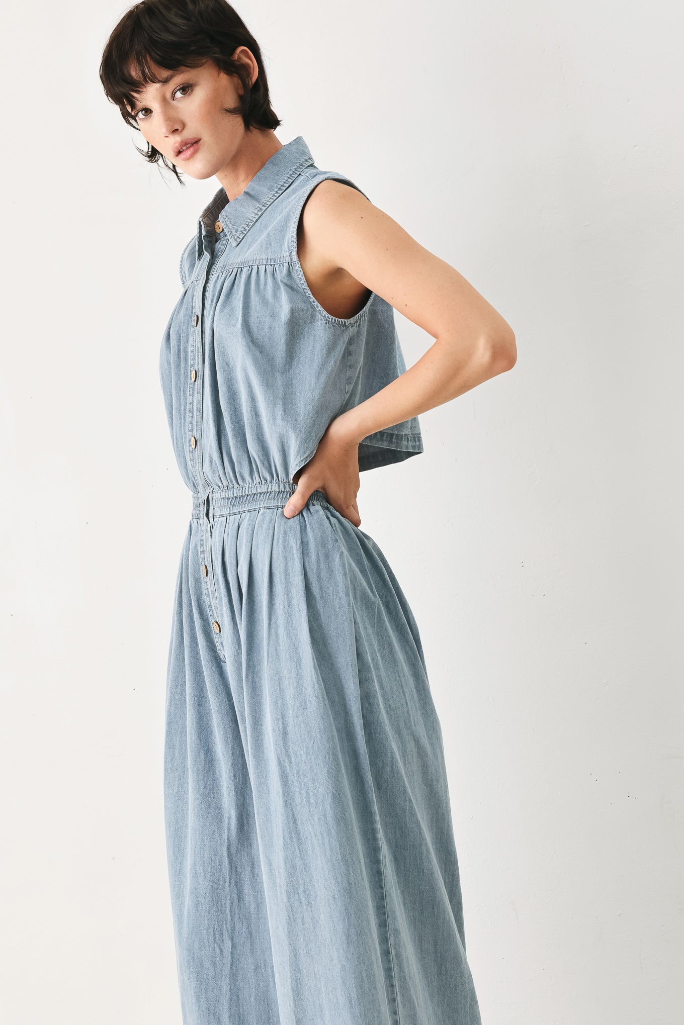 Woman wearing a light blue denim jumpsuit featuring collar, front button down, sleeveless, wide leg, elastic back waistband and popover | FREEMARKET