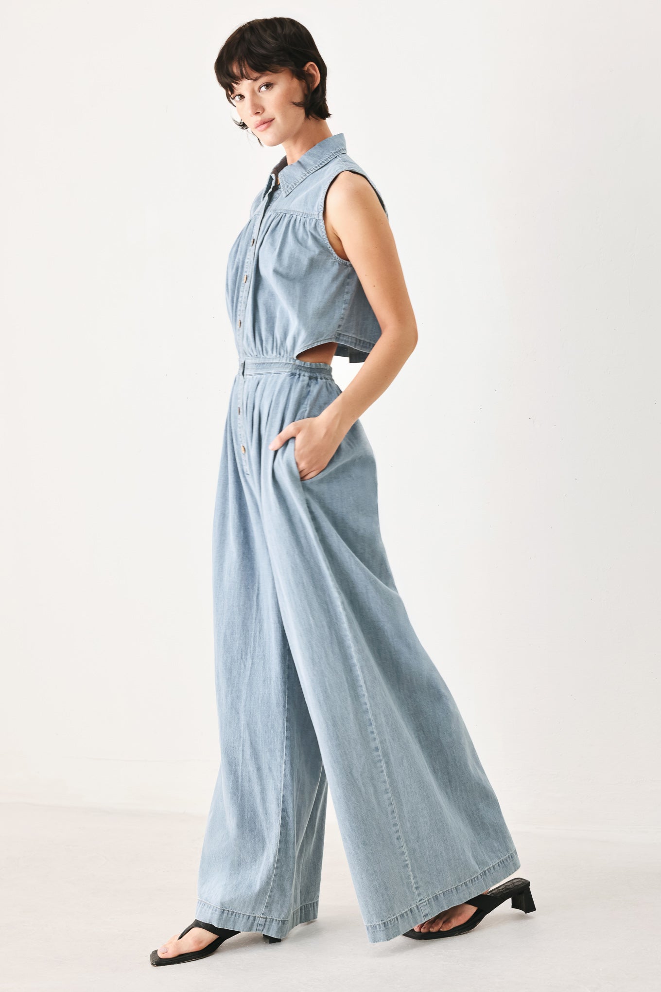 Woman wearing a light blue denim jumpsuit featuring collar, front button down, sleeveless, wide leg, elastic back waistband and popover | FREEMARKET
