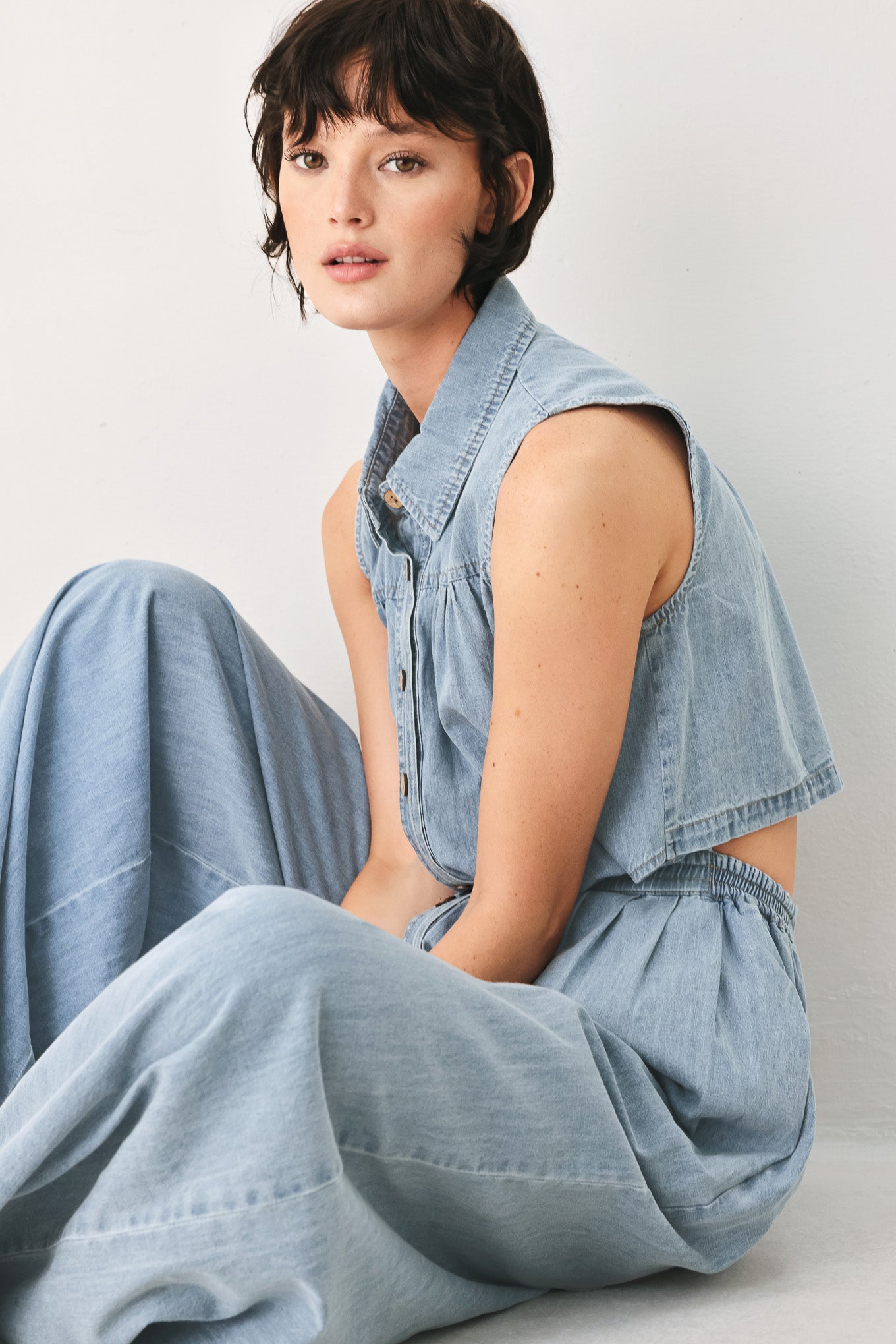 Woman wearing a light blue denim jumpsuit featuring collar, front button down, sleeveless, wide leg, elastic back waistband and popover | FREEMARKET
