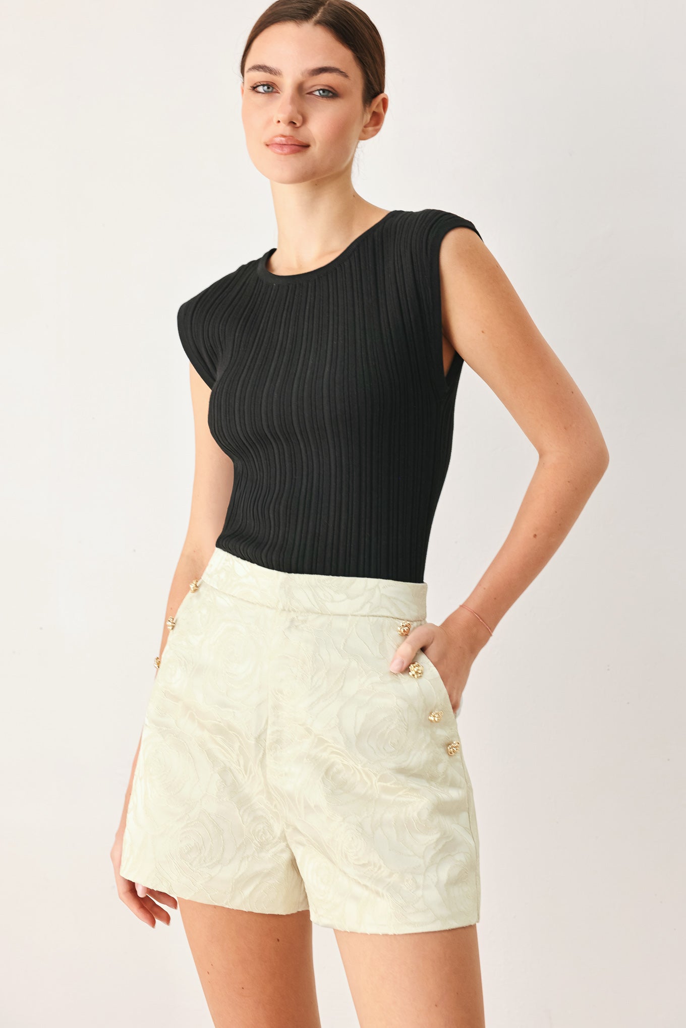 Woman wearing high-waisted cream shorts with a subtle embossed swirl pattern and decorative gold-tone buttons down the side pocket | FREEMARKET