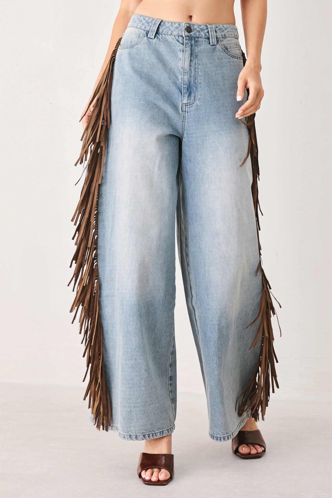A model wearing light-wash blue wide-leg denim jeans with long brown fringe detailing running down the outer sides | FREEMARKET
