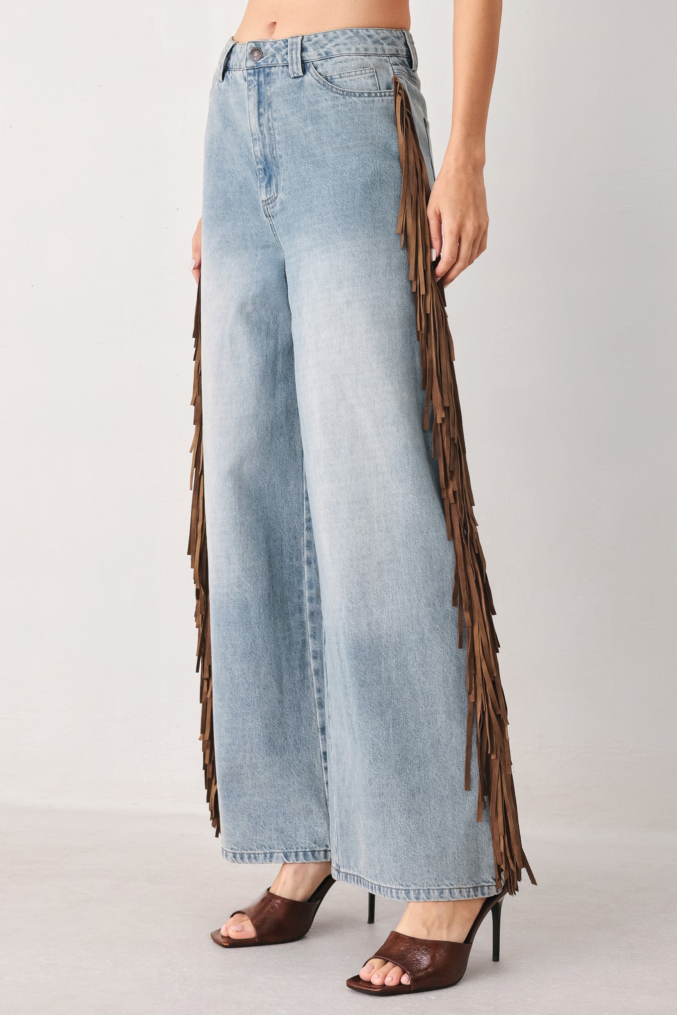 A model wearing light-wash blue wide-leg denim jeans with long brown fringe detailing running down the outer sides | FREEMARKET