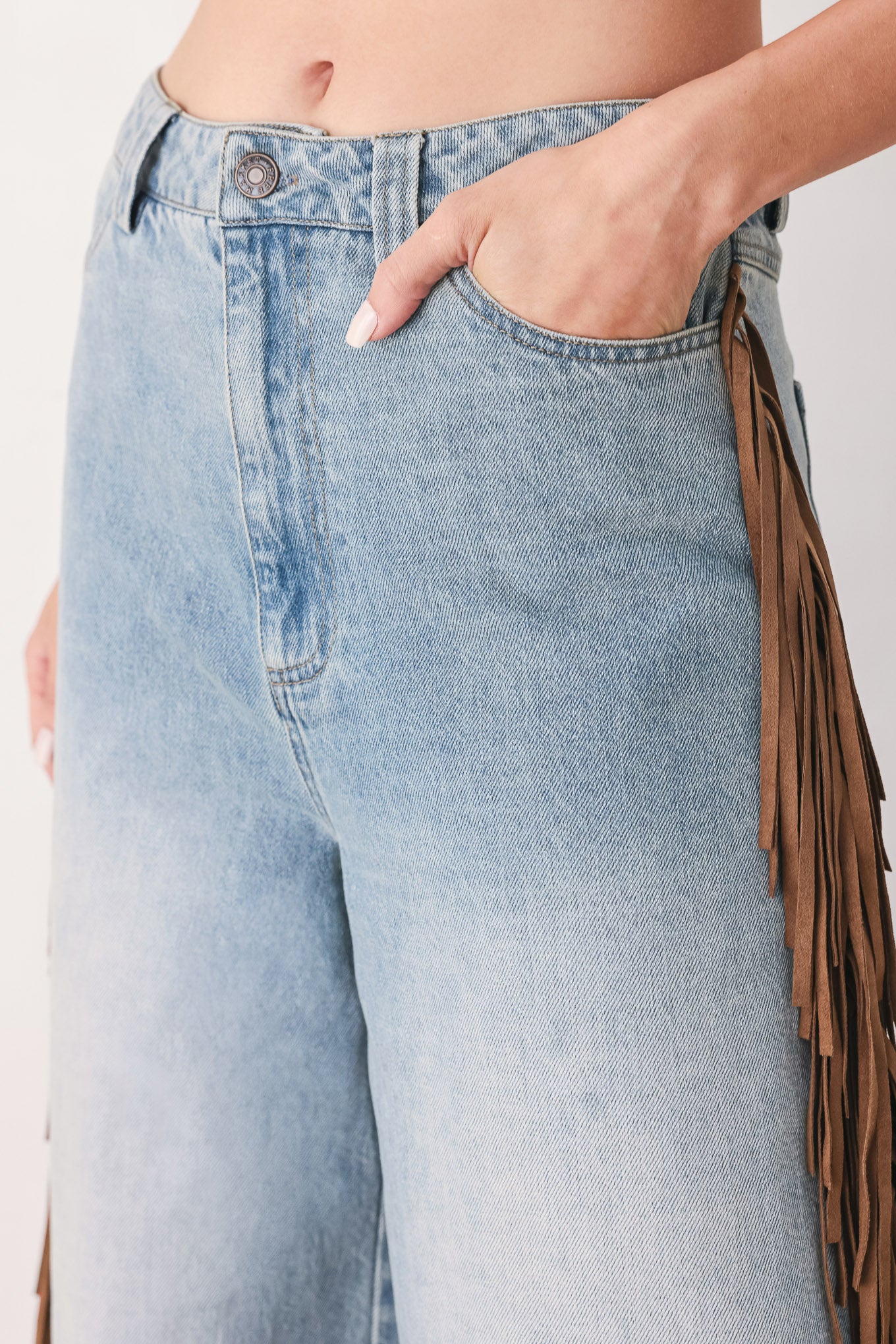 A model wearing light-wash blue wide-leg denim jeans with long brown fringe detailing running down the outer sides | FREEMARKET