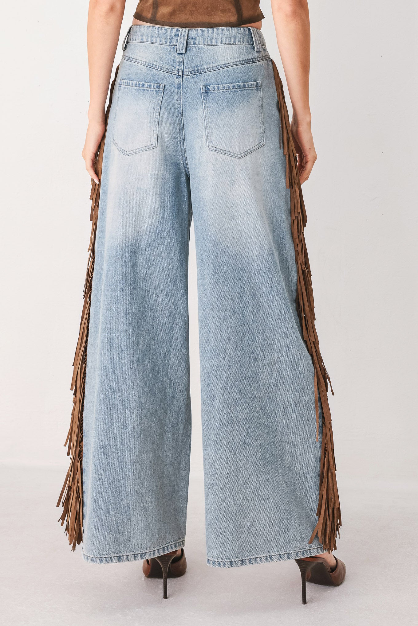 A model wearing light-wash blue wide-leg denim jeans with long brown fringe detailing running down the outer sides | FREEMARKET
