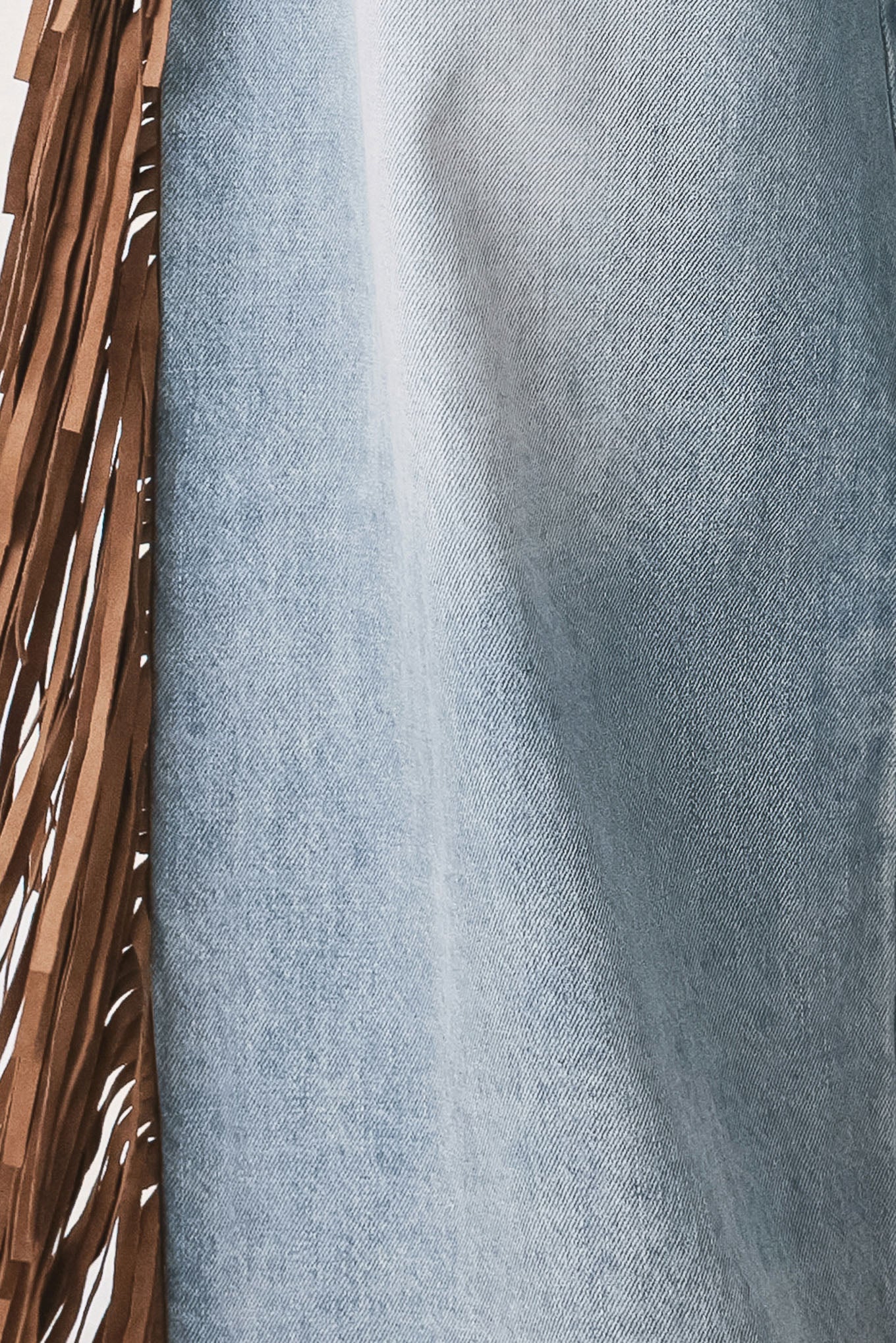 A model wearing light-wash blue wide-leg denim jeans with long brown fringe detailing running down the outer sides | FREEMARKET