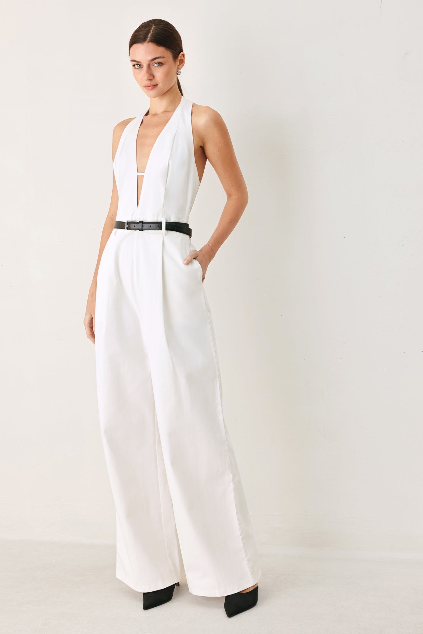 Woman wearing a white jumpsuit with a black belt on a plain background