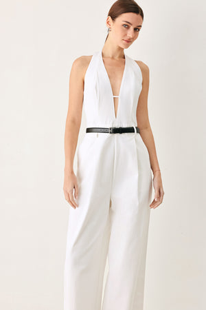 Woman wearing a white woven jumpsuit featuring halter neckline with plunging V front, contrasting belt, single pleat pant with side pocket and bare back with zipper closure | FREEMARKET