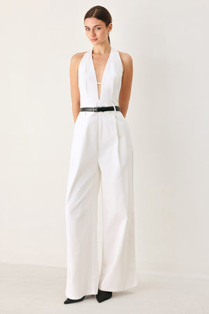 Woman wearing a white woven jumpsuit featuring halter neckline with plunging V front, contrasting belt, single pleat pant with side pocket and bare back with zipper closure | FREEMARKET