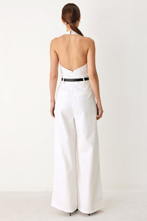 Woman wearing a white woven jumpsuit featuring halter neckline with plunging V front, contrasting belt, single pleat pant with side pocket and bare back with zipper closure | FREEMARKET
