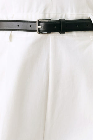 Woman wearing a white woven jumpsuit featuring halter neckline with plunging V front, contrasting belt, single pleat pant with side pocket and bare back with zipper closure | FREEMARKET