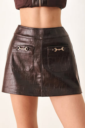 A dark brown faux-crocodile leather mini skort with two front flap pockets featuring horsebit hardware, shown on a model | FREEMARKET