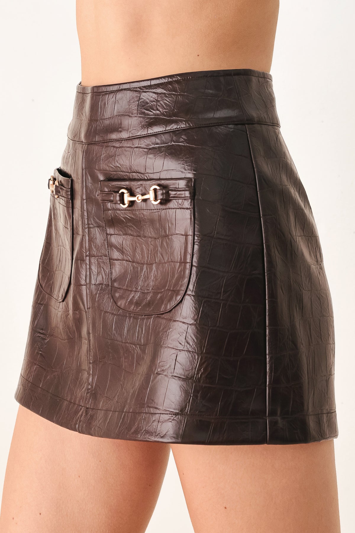 A dark brown faux-crocodile leather mini skort with two front flap pockets featuring horsebit hardware, shown on a model | FREEMARKET