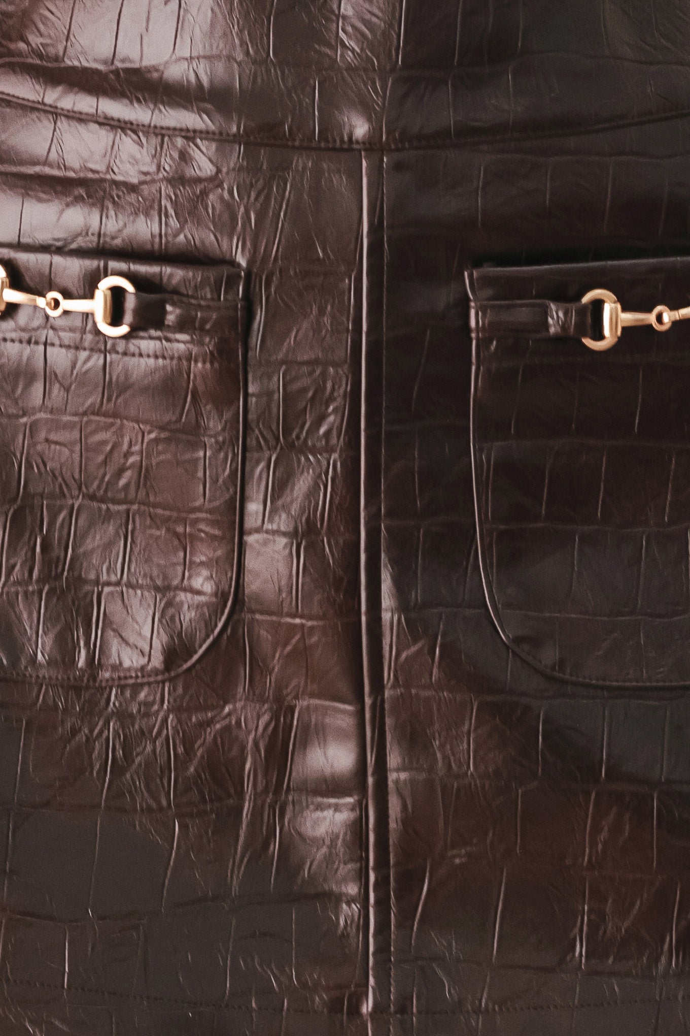 A dark brown faux-crocodile leather mini skort with two front flap pockets featuring horsebit hardware, shown on a model | FREEMARKET