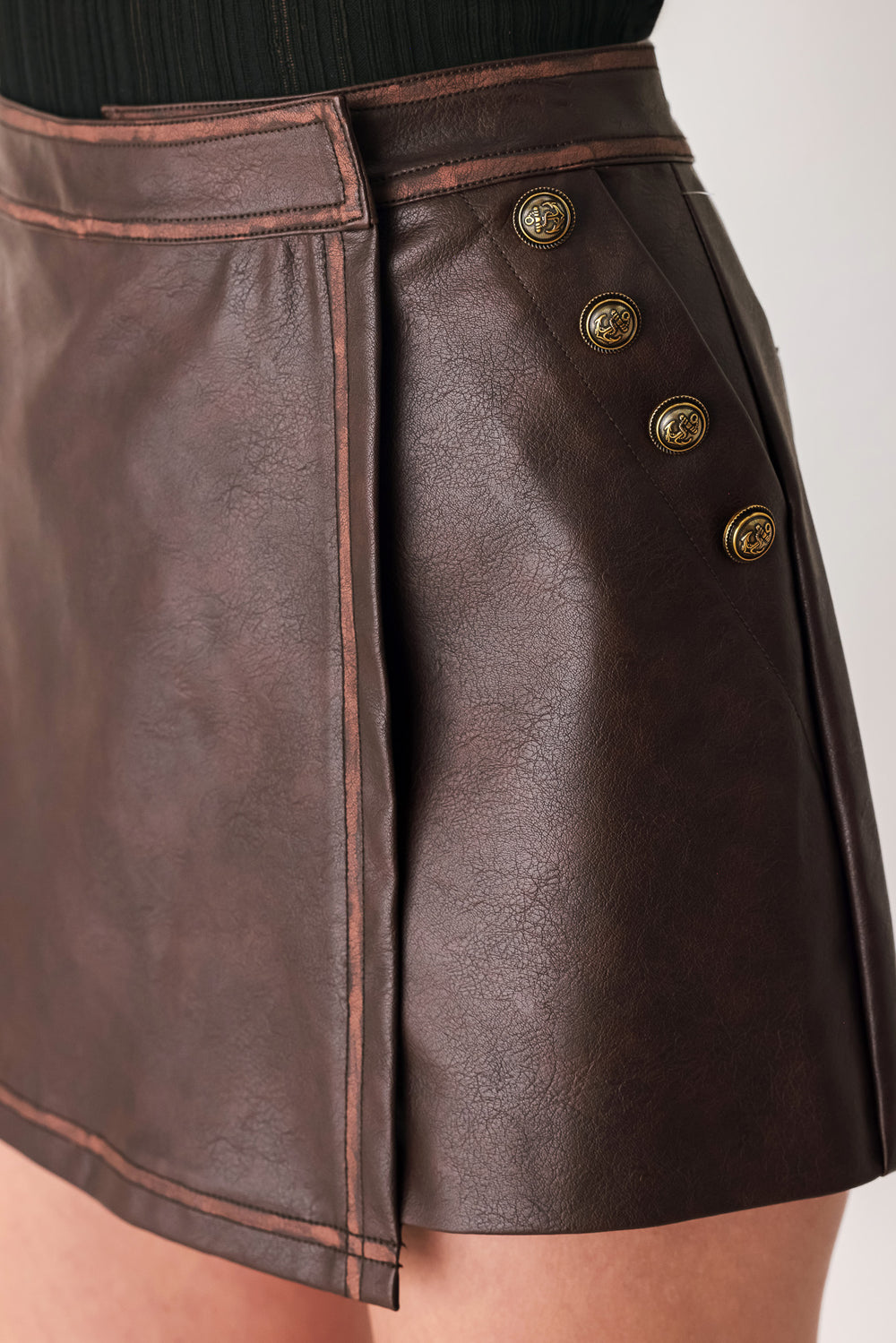 Woman wearing a brown faux leather skort with buttons along the pocket seam | FREEMARKET