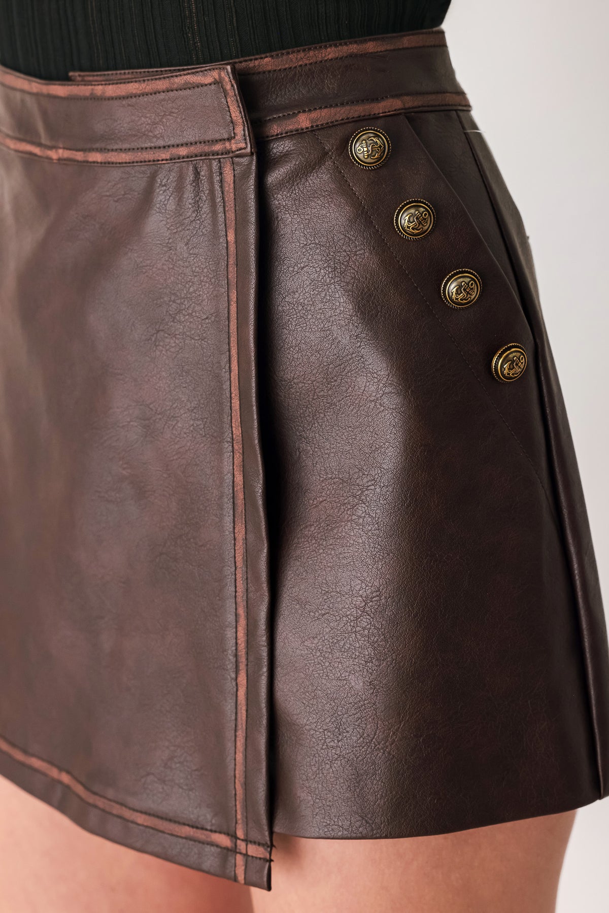 Woman wearing a brown faux leather skort with buttons along the pocket seam | FREEMARKET