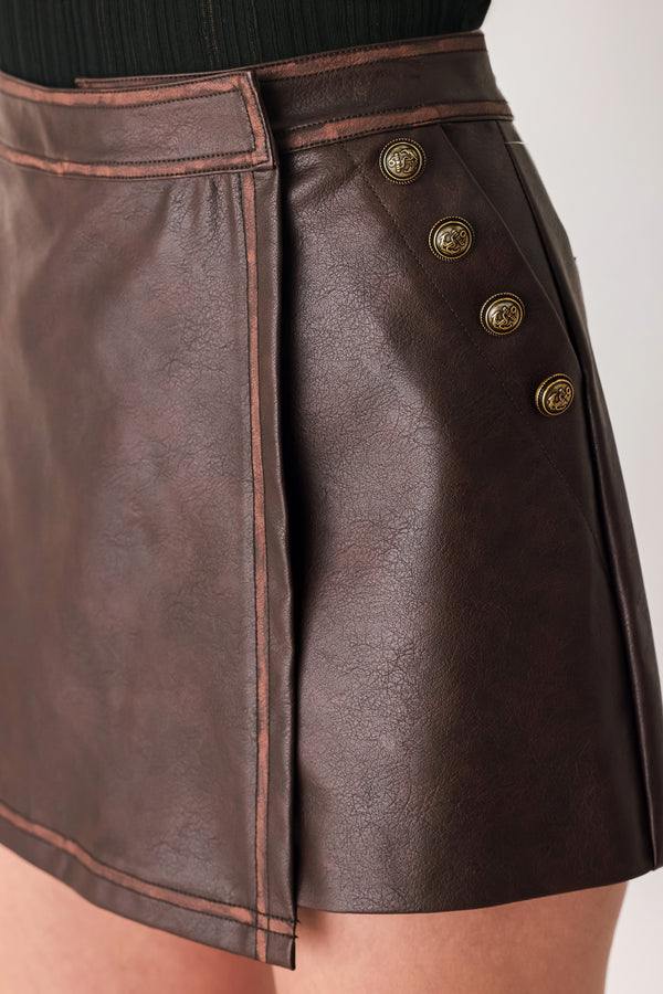 Woman wearing a brown faux leather skort with buttons along the pocket seam | FREEMARKET