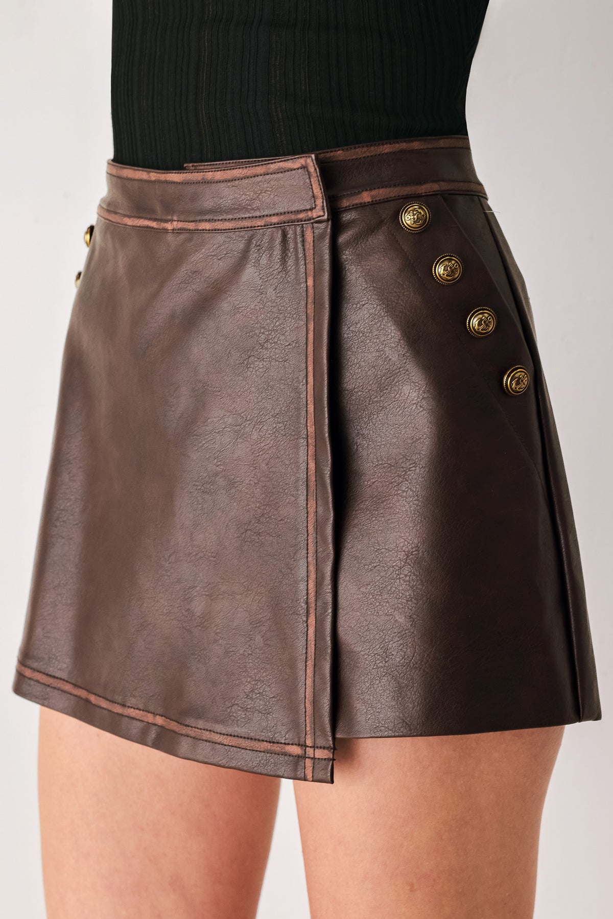 Woman wearing a brown faux leather skort with buttons along the pocket seam | FREEMARKET