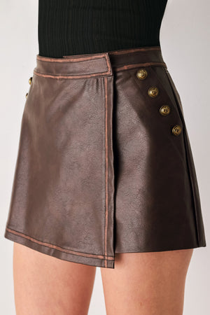 Woman wearing a brown faux leather skort with buttons along the pocket seam | FREEMARKET