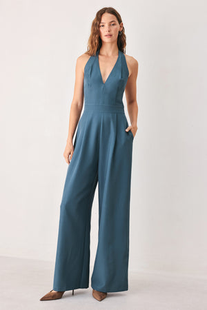 A woman modeling a teal blue halter-neck wide-leg jumpsuit with a deep V-neckline and side pockets | FREEMARKET