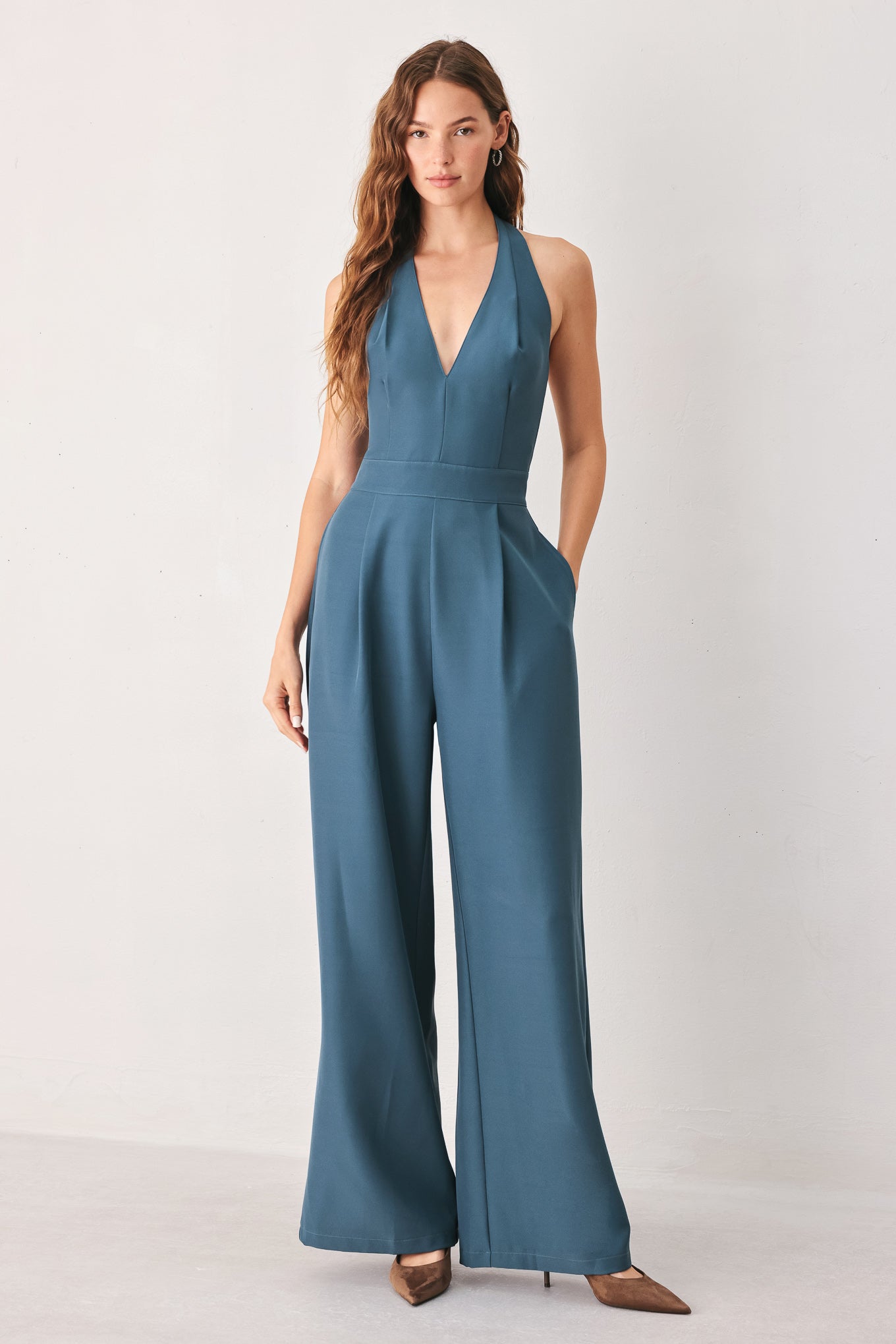 A woman modeling a teal blue halter-neck wide-leg jumpsuit with a deep V-neckline and side pockets | FREEMARKET