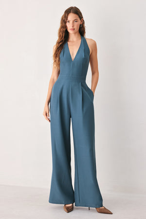 A woman modeling a teal blue halter-neck wide-leg jumpsuit with a deep V-neckline and side pockets | FREEMARKET