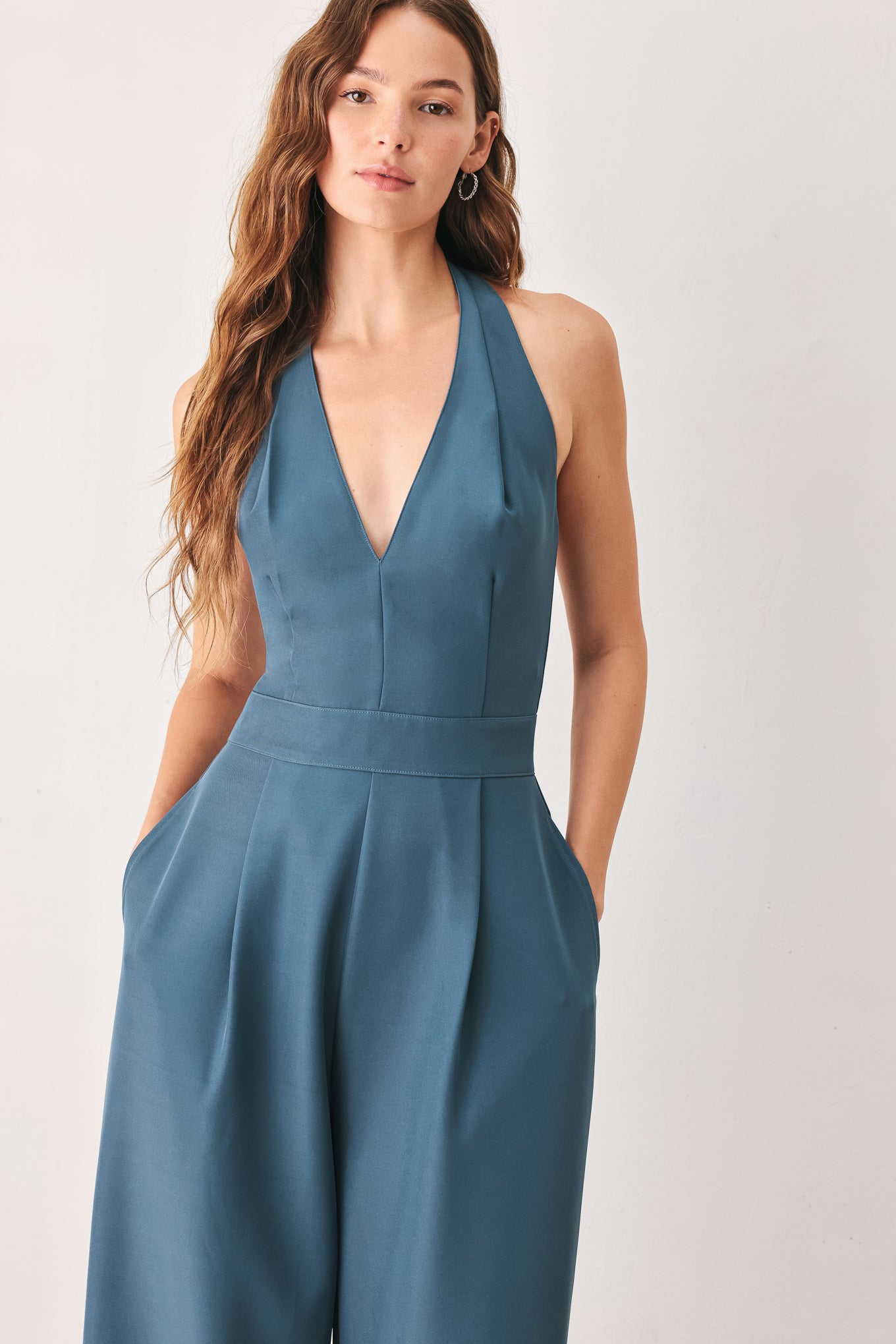 A woman modeling a teal blue halter-neck wide-leg jumpsuit with a deep V-neckline and side pockets | FREEMARKET