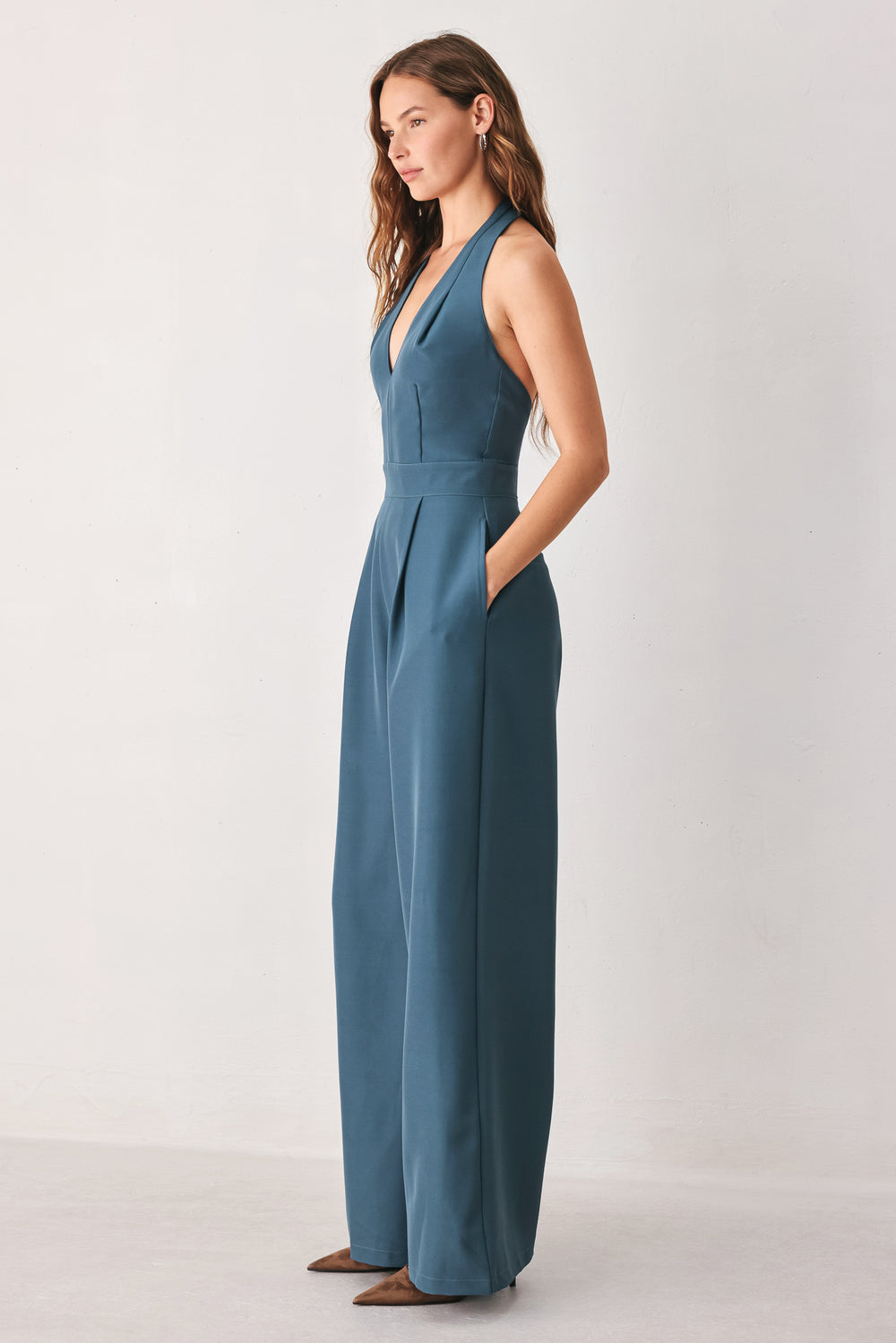 A woman modeling a teal blue halter-neck wide-leg jumpsuit with a deep V-neckline and side pockets | FREEMARKET