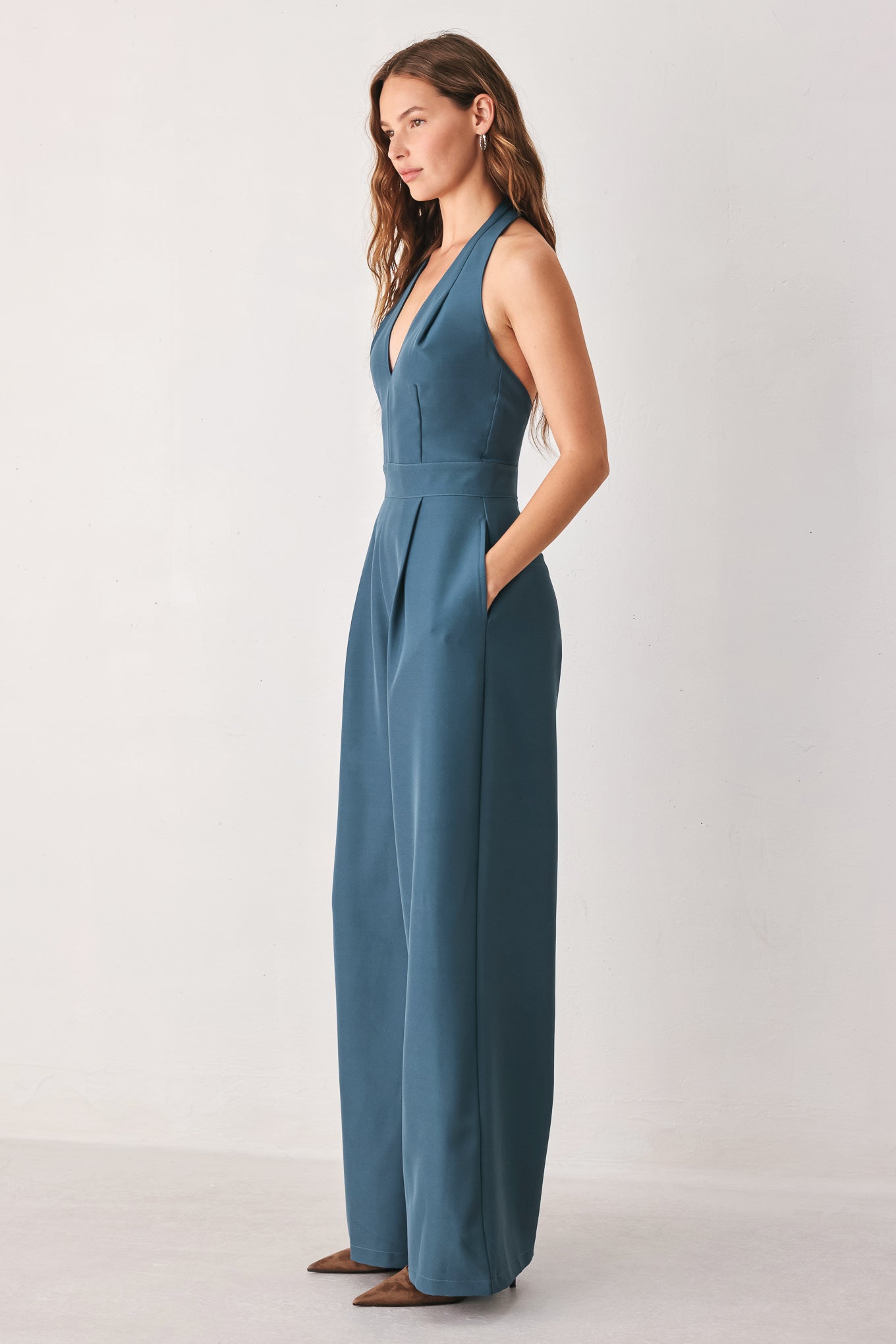 A woman modeling a teal blue halter-neck wide-leg jumpsuit with a deep V-neckline and side pockets | FREEMARKET